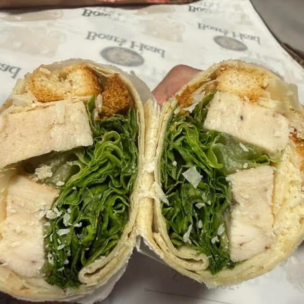 A chicken Caesar salad wrap, cut in half, revealing chicken, lettuce, croutons, and cheese.