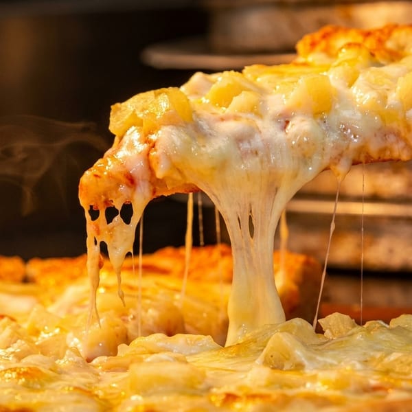 A hot slice of pineapple pizza with melted cheese stretching from the pie.