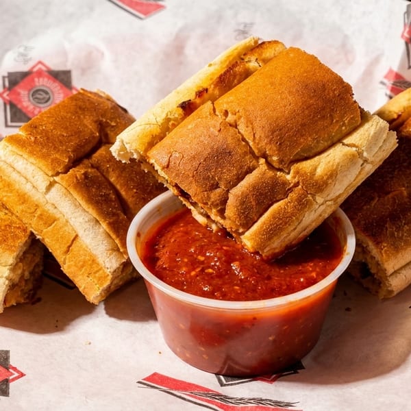 Toasted breadsticks with a side of marinara sauce, served in a paper-lined basket.